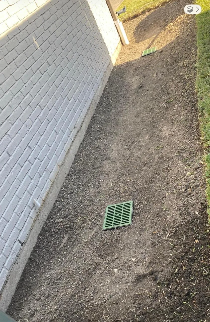 Catch basin positioned beside a residential foundation in a graded soil strip