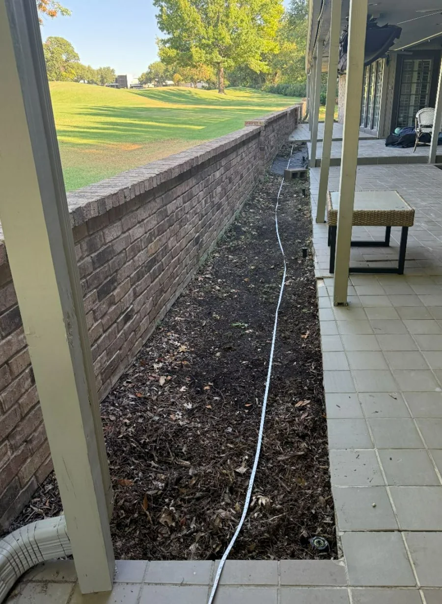 Narrow outdoor area between a covered patio and fence evaluated for standing water