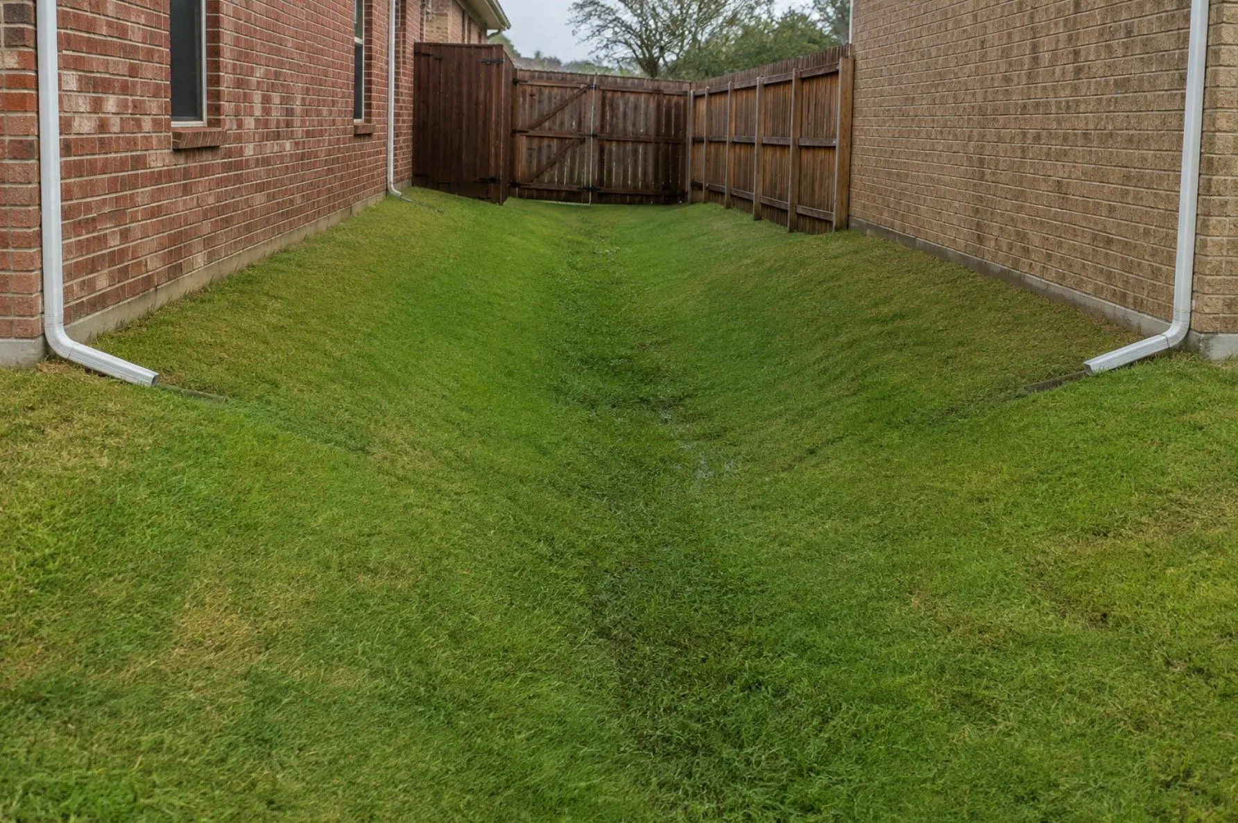 A low grassy corridor between two brick homes where runoff can collect