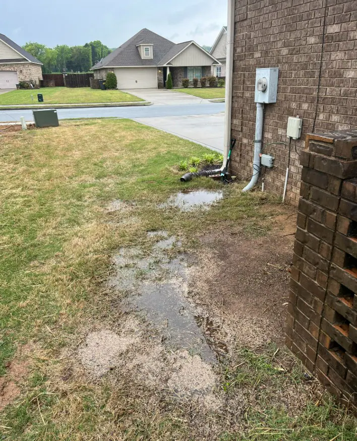 Soggy muddy ground and shallow water beside a brick home
